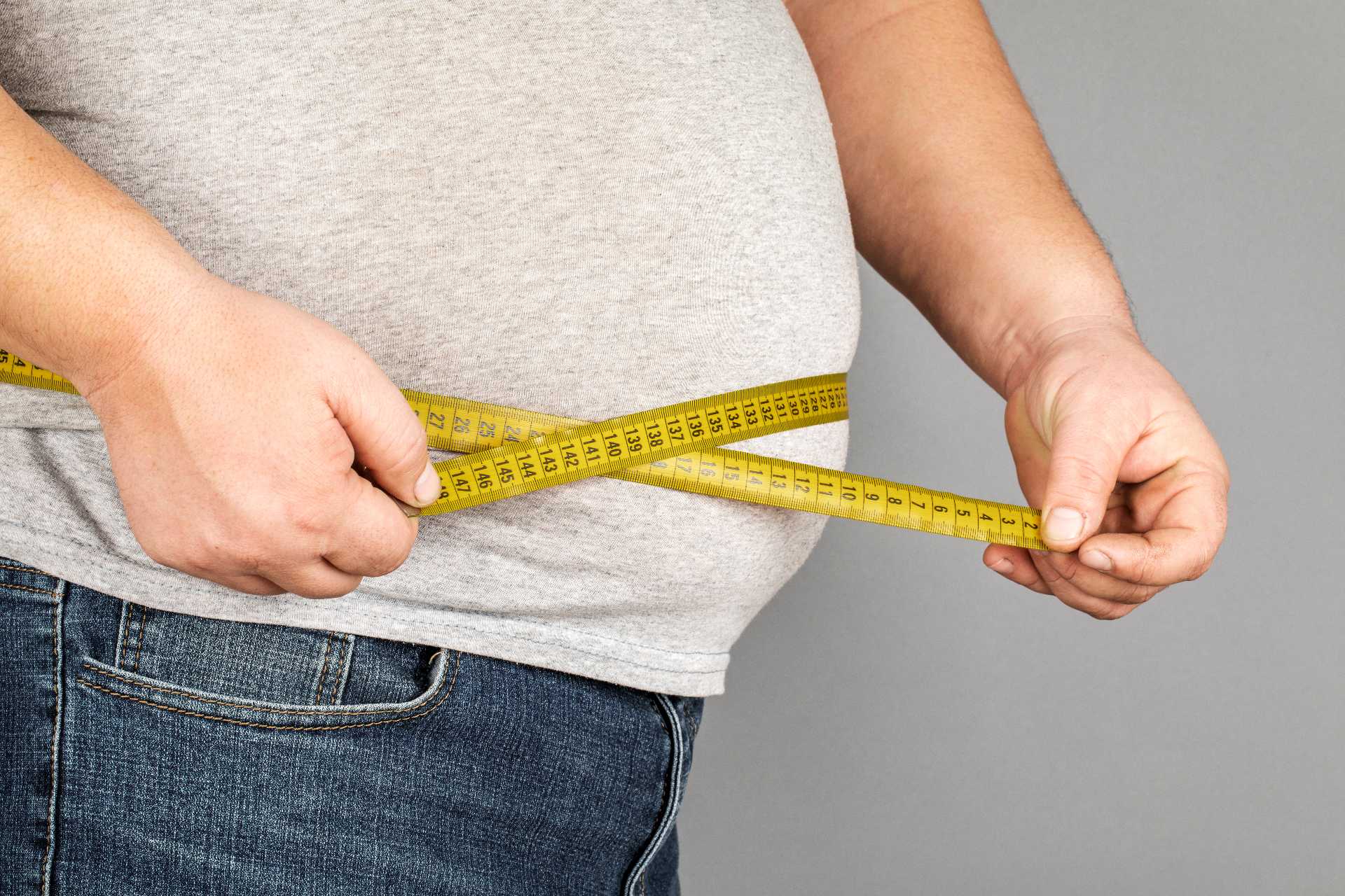Hombre con sobrepeso midiendo su abdomen con una cinta métrica.